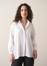 Woman wearing an oversized white shirt and dark jeans on a beige background