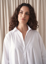 Woman wearing a white oversized shirt with beige fabric backdrop