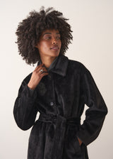 Close up of women wearing an oversized black faux fur coat, on a beige background
