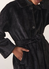 Close up of an oversized black faux fur coat, buttoned up with woman's hand in pocket
