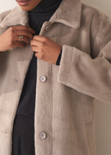 Close up of woman buttoning up a an oversized oatmeal faux fur coat over a black knitted sweater