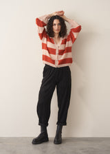 Woman wearing a red and blush pink striped cardigan with black trousers and chunky boots