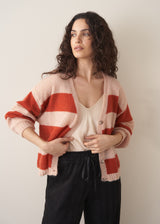 Woman wearing a red and blush pink striped cardigan over white satin top and black drawstring trousers