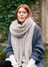 Woman outdoors, wearing a Hazel chunky knit wool blend scarf in a neutral tone, styled over a slate grey cardigan