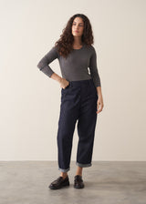 Woman wearing a grey metallic long-sleeve top and dark jeans against a beige background