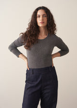 Woman wearing a grey metallic long-sleeve top and dark jeans against a beige background