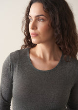 Woman wearing a grey metallic long-sleeve top and dark jeans against a beige background