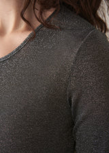 Woman wearing a grey metallic long-sleeve top and dark jeans against a beige background