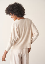 A woman wearing a light oatmeal cream knit cardigan over a white V-neck top and matching light oatmeal trousers.