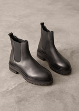 Pair of ankle length black leather Chelsea boots on a gray concrete surface