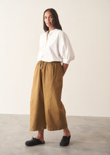Woman wearing mustard yellow, olive green oversized barrel leg trousers with a white cotton shirt and black shoes.