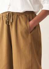 Woman wearing mustard yellow, olive green oversized barrel leg trousers with a white cotton shirt and black shoes.