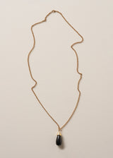 A long golden chain with a chunky black oval pendant, photographed against a simple beige background
