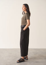 Woman wearing a striped t-shirt and black linen trousers, standing against a plain wall.