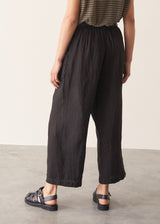 Woman wearing a striped t-shirt and black linen trousers, standing against a plain wall.