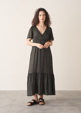 Woman wearing a long, dark patterned dress against a plain background