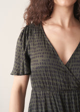 Woman wearing a green patterned dress with a plain background