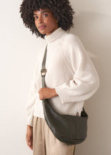 Woman holding a khaki leather bag against a plain background