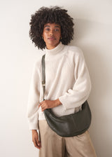 Woman holding a khaki leather bag against a plain background