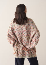 Woman wearing a multicoloured oversized cardigan and jeans against a plain background