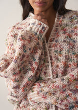 Woman wearing a multicoloured oversized cardigan and jeans against a plain background