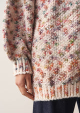 Woman wearing a multicoloured oversized cardigan and jeans against a plain background