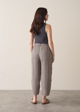 Woman modelling grey checked cropped linen barrel leg trousers a grey vest top and sandals, against a beige background