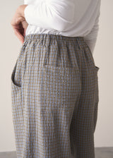 Woman wearing cotton seersucker checked barrel leg trousers and a white top.
