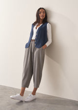 Woman wearing a blue linen waistcoat, white shirt, and cotton checked trousers.