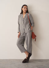 A woman models a blue-green checked cotton jacket over a white shirt, paired with matching cropped barrel-leg trousers, bag and loafers, set against a beige background