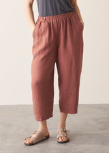 Person wearing rust-coloured cropped barrel-leg trousers on a plain background