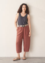 Woman wearing a sleeveless top and terracotta cropped barrel-leg trousers against a plain background