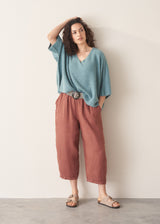 Woman wearing a blue top and terracotta cropped barrel-leg trousers against a plain background