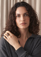 Woman wearing a brown heart tortoiseshell ring with grey polo neck sweater, against a beige fabric background