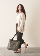 Woman holding a textured gray tote bag against a plain background
