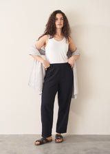 Woman wearing a white top and black pants against a plain background