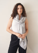Woman wearing a light gray scarf and black pants against a plain background