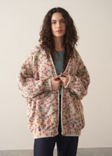 Woman wearing a space dye patterned oversized cardigan and blue jeans against a plain background