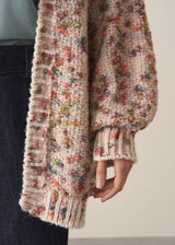 Woman wearing a space dye patterned oversized cardigan and blue jeans against a plain background