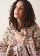 Woman wearing a space dye patterned oversized cardigan and blue jeans against a plain background