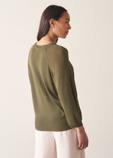 Woman wearing olive green v-neck sweater and pale trousers