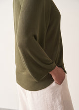 Woman wearing olive green v-neck sweater and pale trousers
