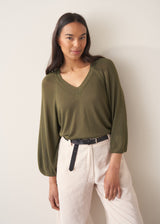 Woman wearing olive green v-neck sweater and pale trousers