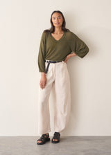 Woman wearing olive green v-neck sweater and pale trousers