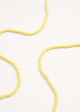 Close up of a long yellow crystal necklace on beige background