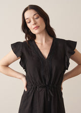 Woman wearing a black linen midi dress with a drawstring waist and embroidery detail against a beige background