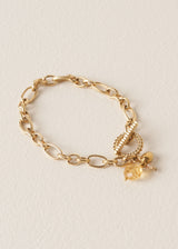 A bracelet with gold interlocking chain, crystals, beads, and t-bar clasp, on a beige background