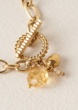 Closeup of bracelet with gold interlocking chain, crystals, beads, and t-bar clasp, on a beige background