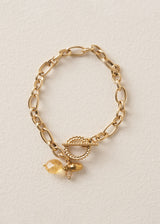 A bracelet with gold interlocking chain, crystals, beads, and t-bar clasp, on a beige background