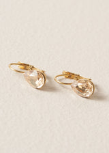 Side view of gold hoop earrings with champagne teardrop crystals on a beige background